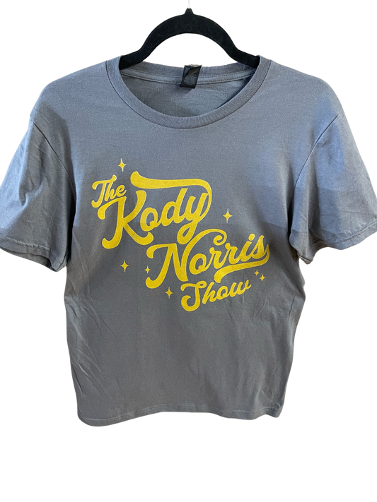 The Kody Norris Show Graphic Tee (Short Sleeve, Color Charcoal)  Gildan Softstyle Tee.   Available in Charcoal with Gold Letting.   All Shirts include a secondary logo on the back collar. 