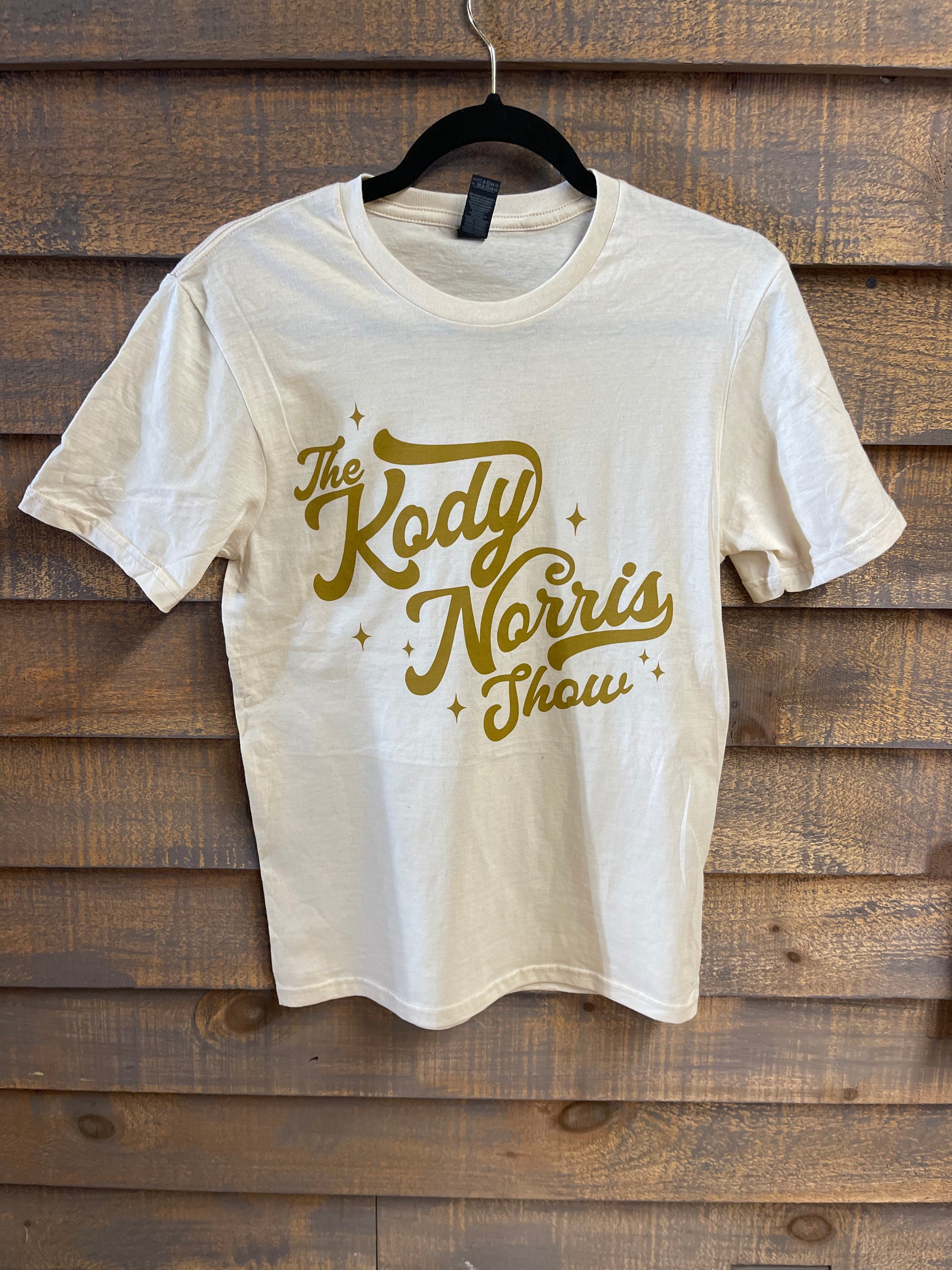 The Kody Norris Show Graphic Tee (Short Sleeve, Color Natural) Gildan Softstyle Tee. Available in Natural with Gold Lettering All Shirts include a secondary logo on the back collar.